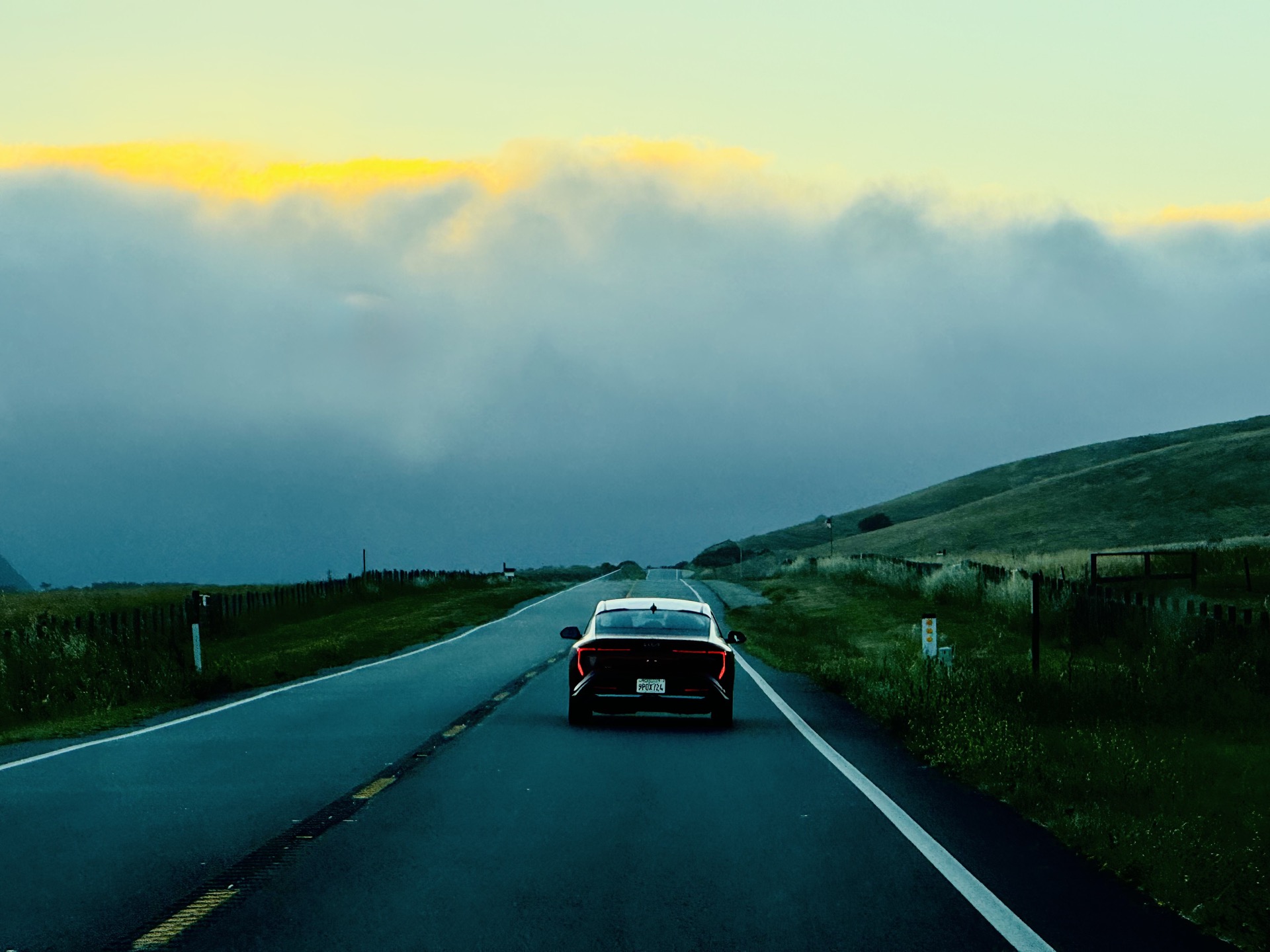 Car driving along 18-Mile Road toward a glowing Pacific horizon